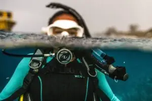 Diver in a wetsuit shown in a split-level shot, half submerged underwater and half above the surface.