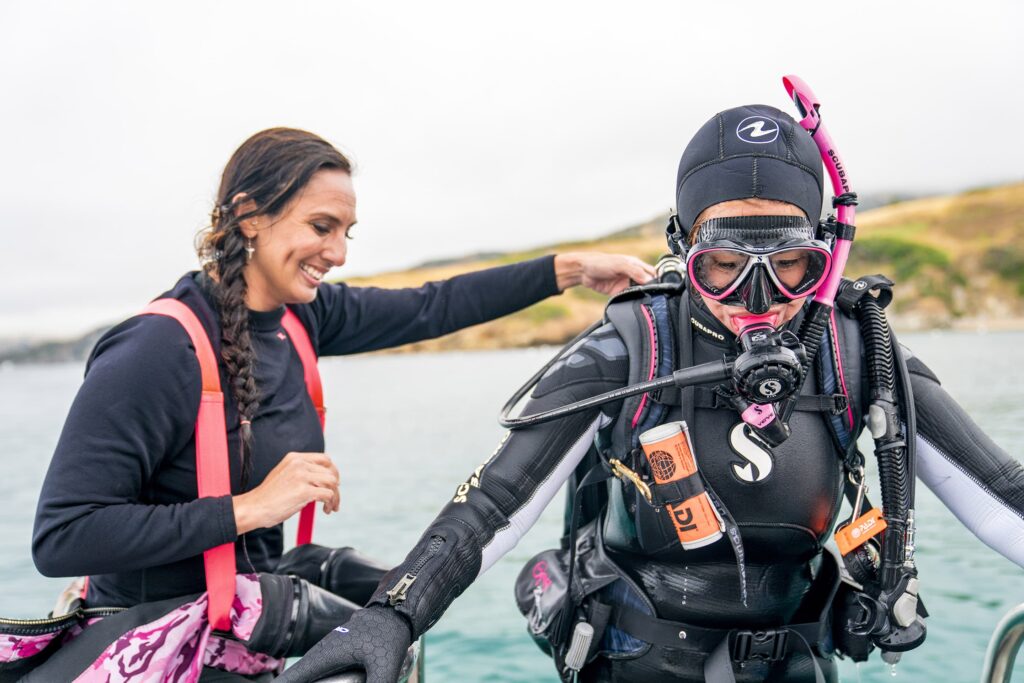 Smiling woman assisting a scuba diver exiting the water onto a boat.
