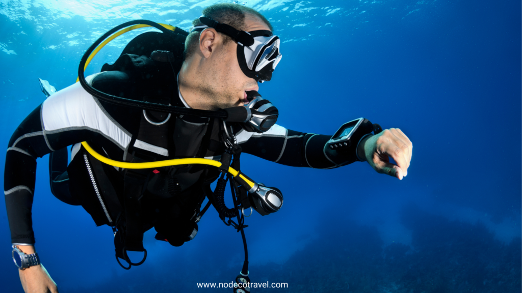 Scuba diver in a wetsuit checking a dive computer underwater in clear blue ocean.